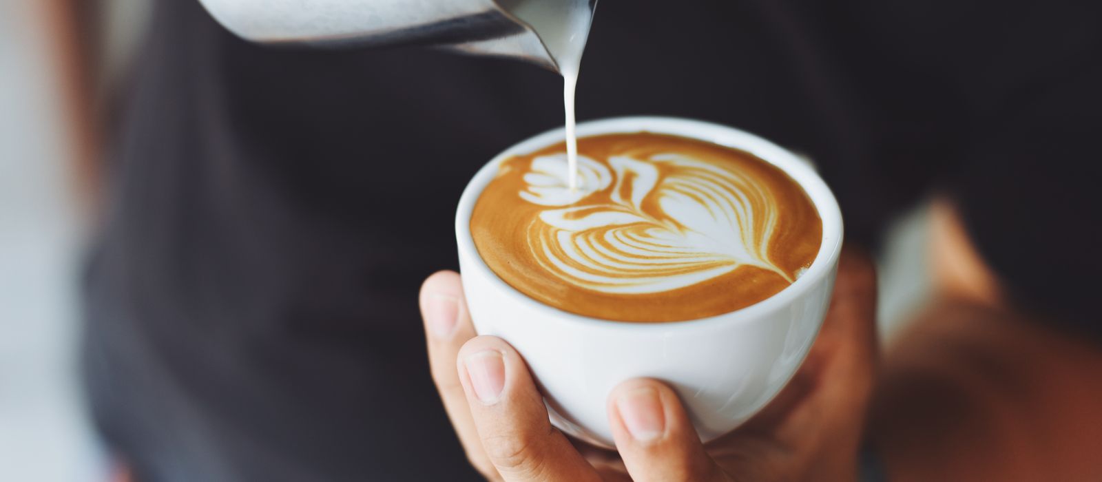 A barista pouring latte art into a cup, coffee shop web design by Designs by Delia