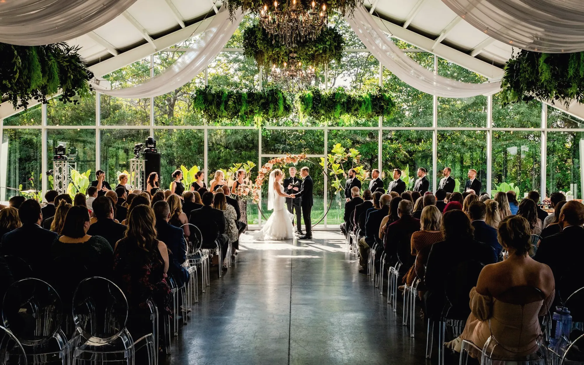 Wedding ceremony in a glass pavilion filled with greenery